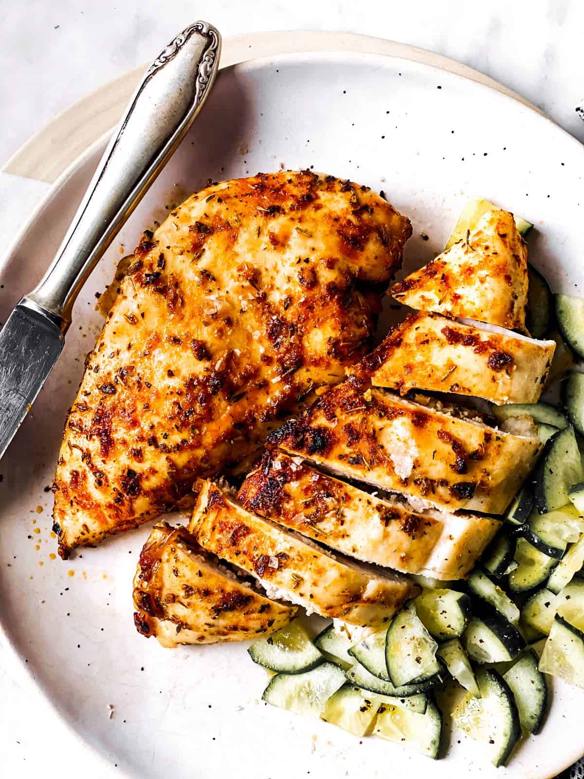 overhead view of sliced airy fryer chicken breasts on white plate with cucumber salad