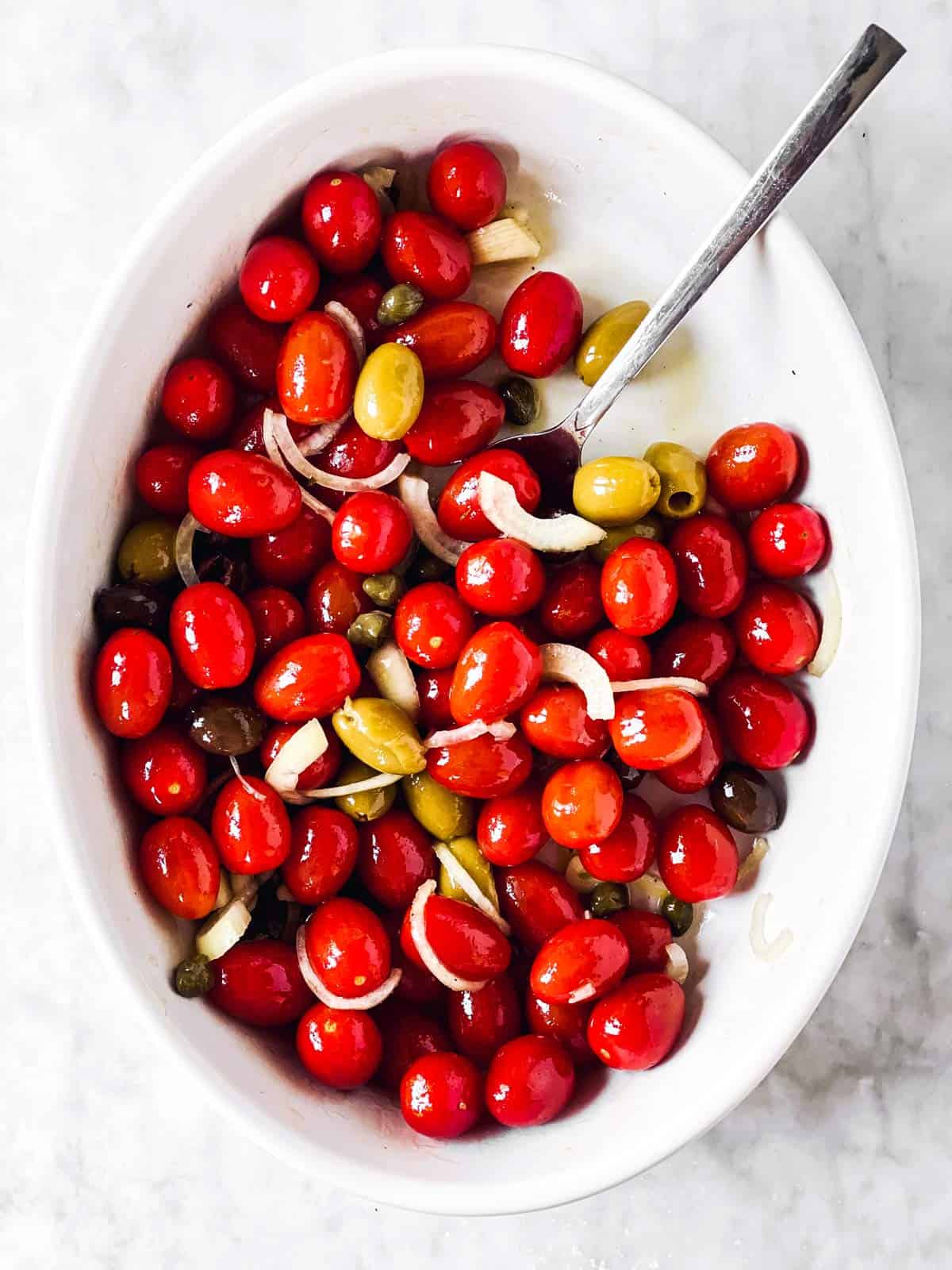 white casserole dish with tomatoes, onions and olives