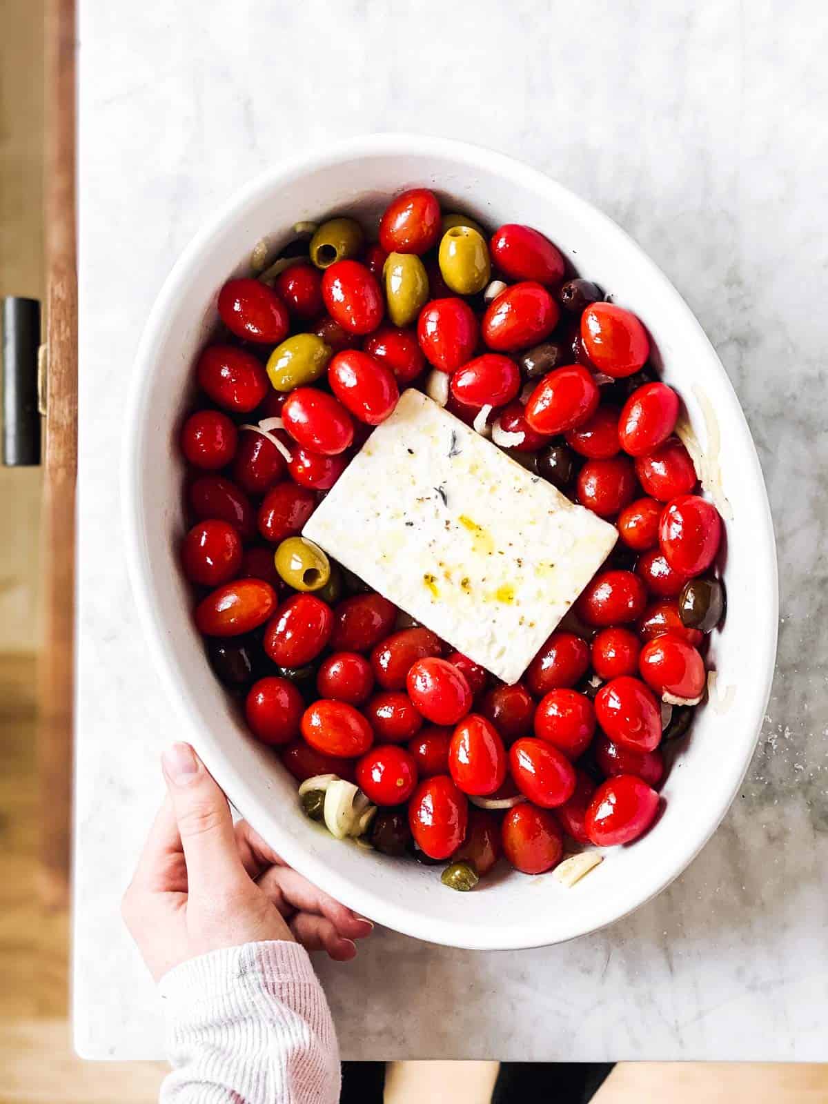 female hand holding dish with feta and tomatoes on countertop