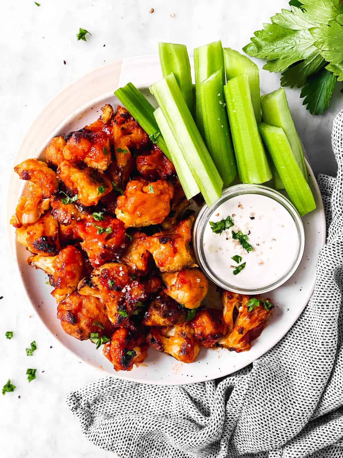 overhead view of white platter with buffalo cauliflower wings, ranch dip and celery sticks