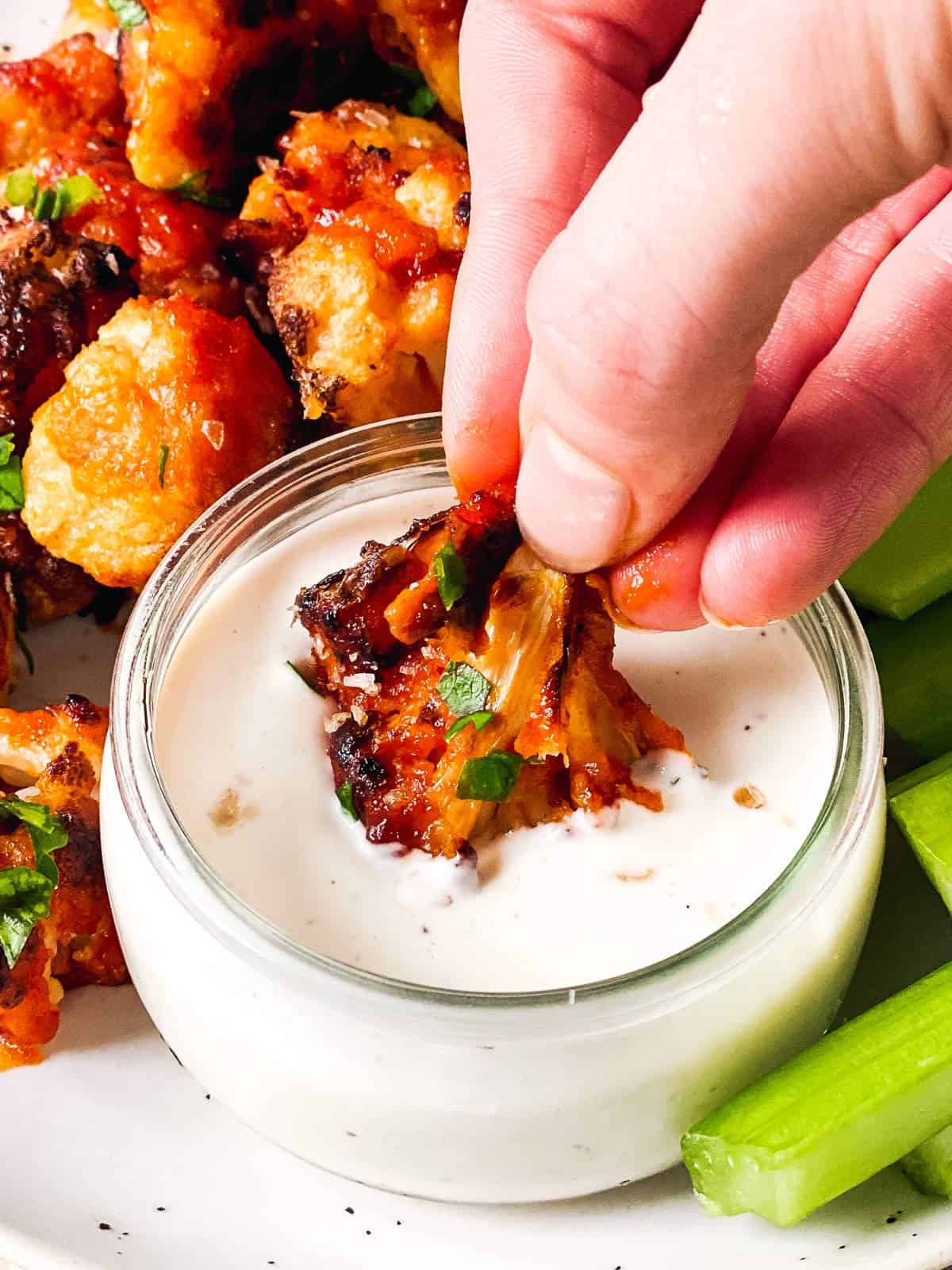 female hand dipping cauliflower wing into ranch dip