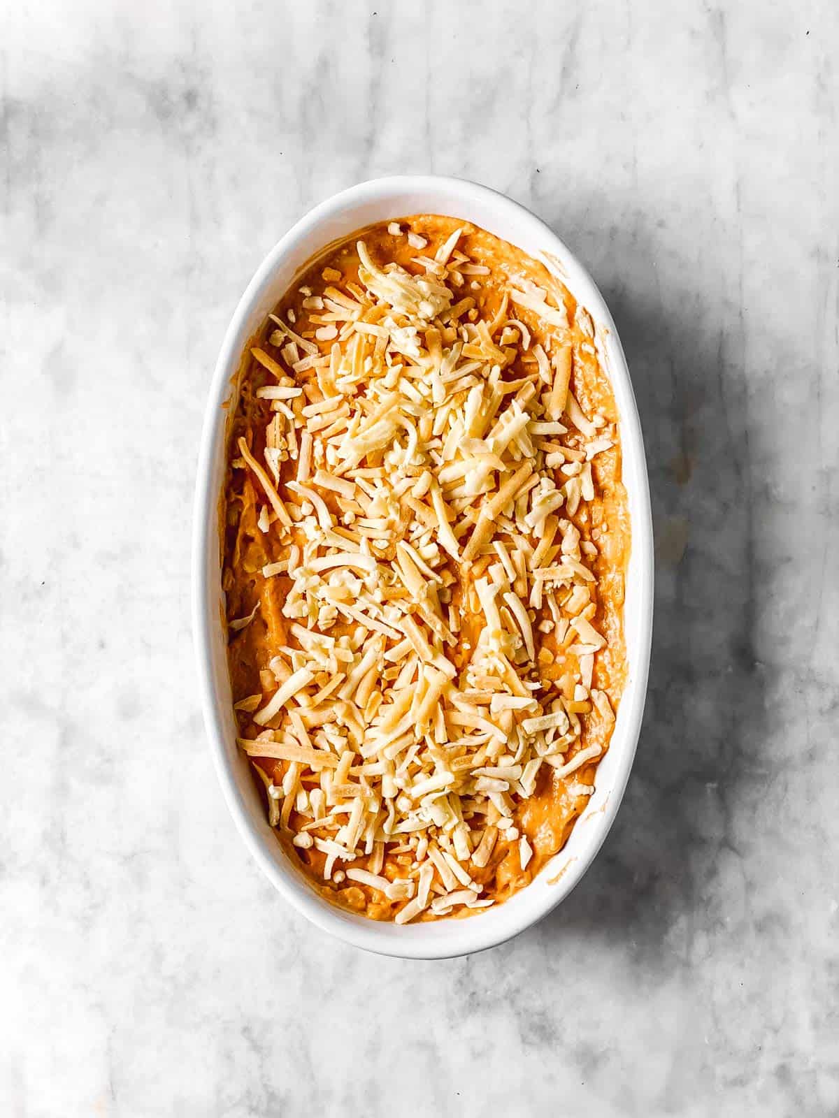 buffalo chicken dip mixture in white dish with cheese sprinkled on