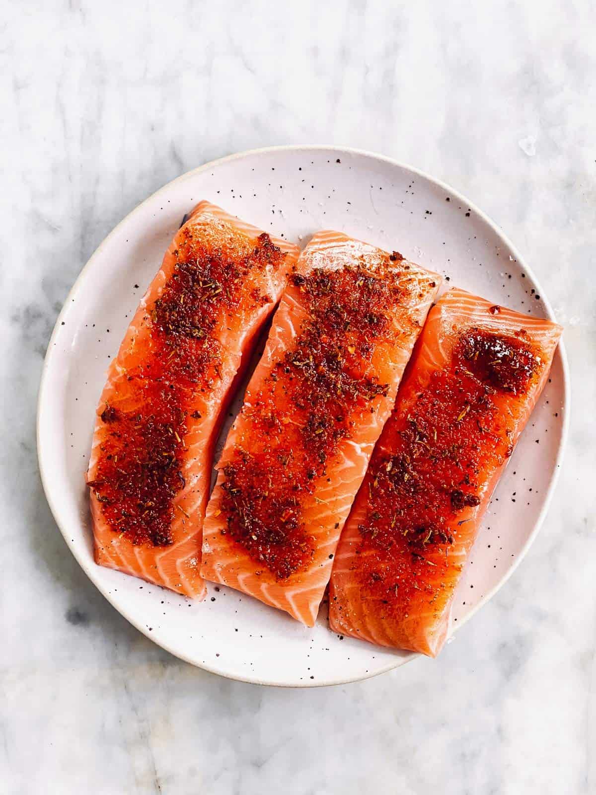 seasoned raw salmon fillets on white plate