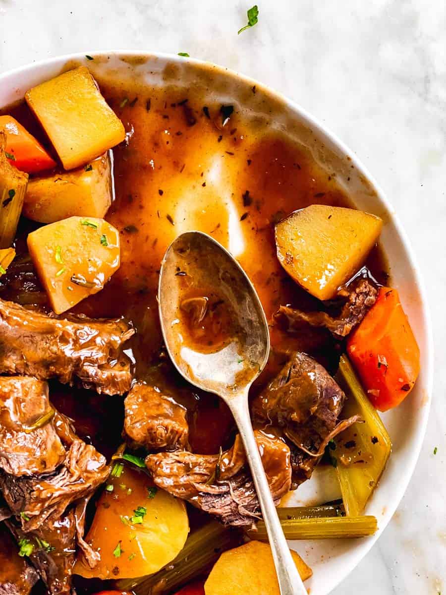 serving spoon on platter with gravy, beef roast and vegetables