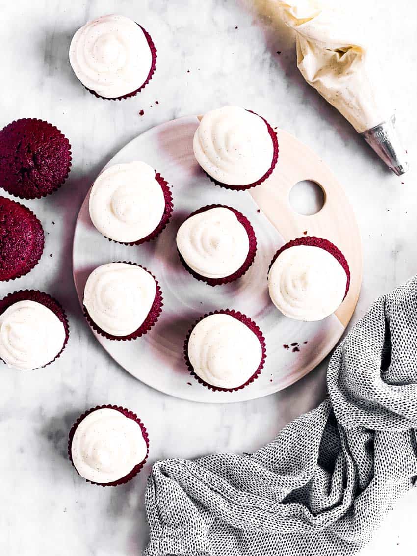 overhead view of red velvet cupcakes on countertop with frosting and piping bag on the side