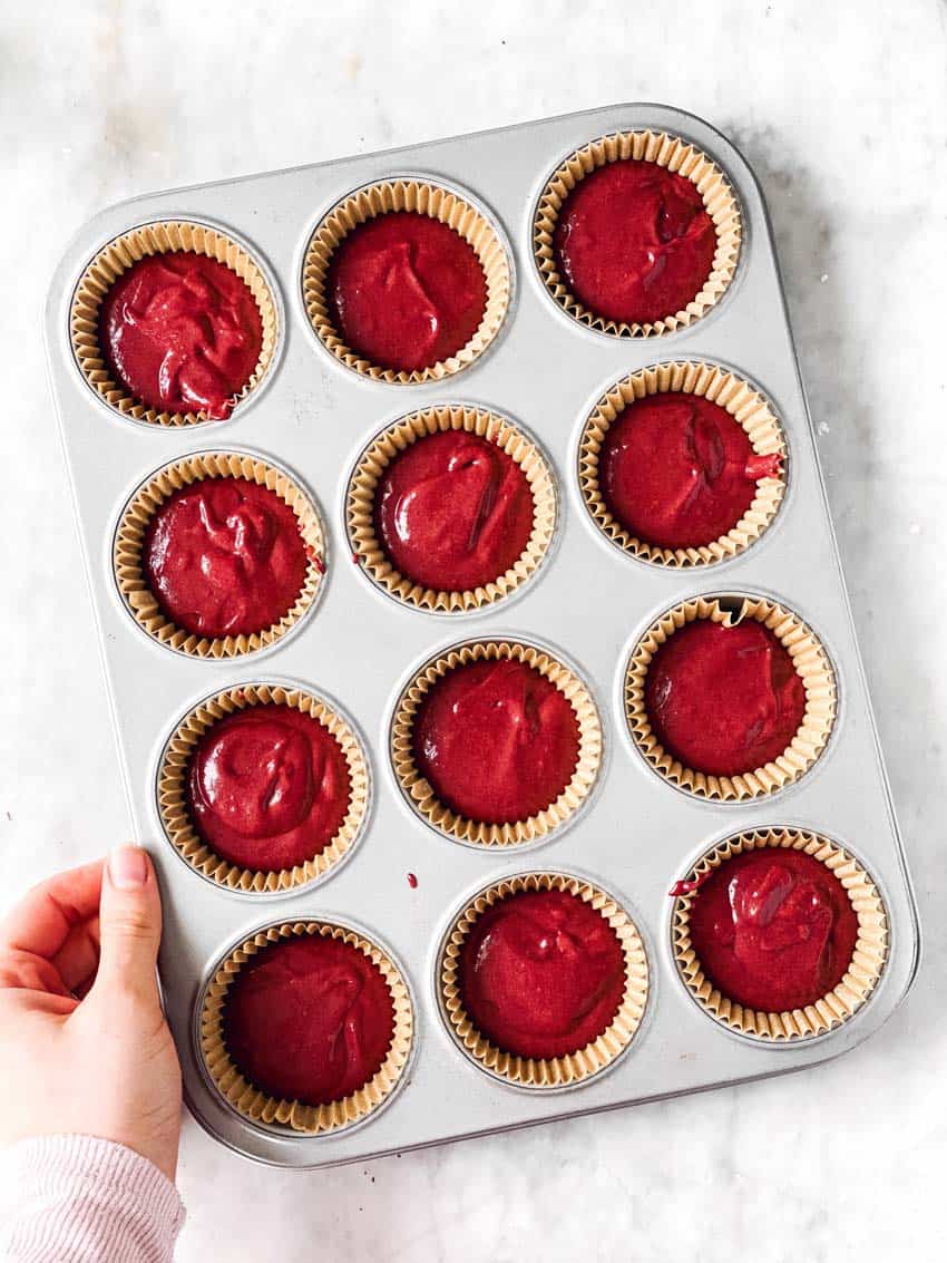 female hand holding muffin pan filled with red velvet cupcake batter