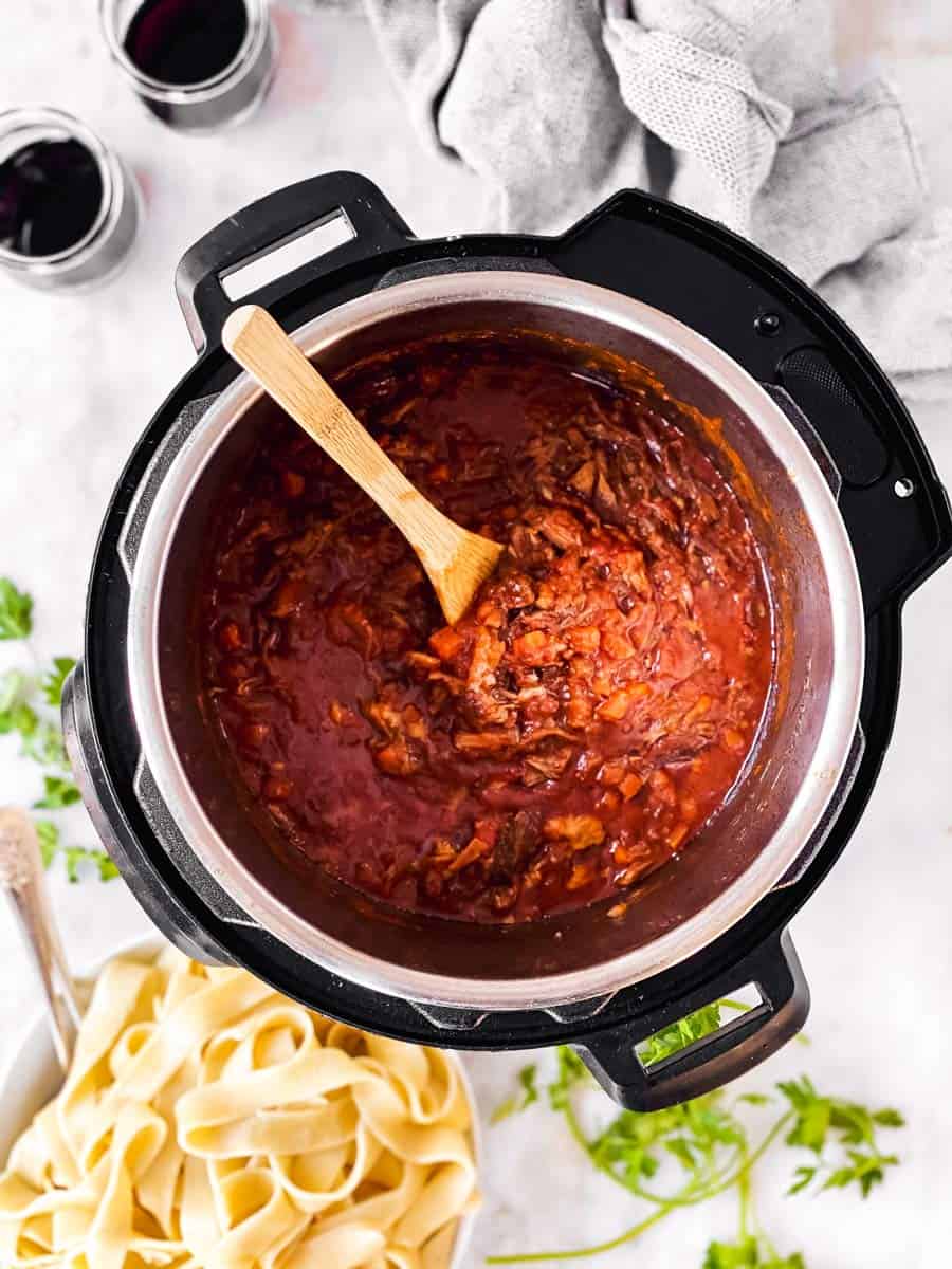 instant pot with short rib ragu next to bowl with pappardelle and glasses of red wine