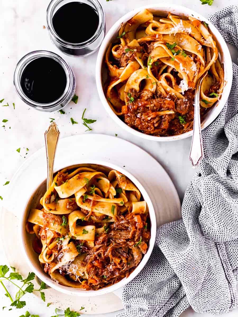 two plates with short rib ragu and pappardelle on marble surface