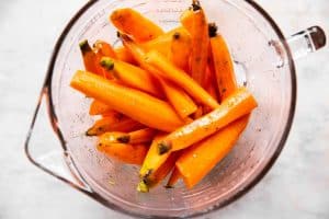 glass bowl with raw carrots tossed in oil and seasoning