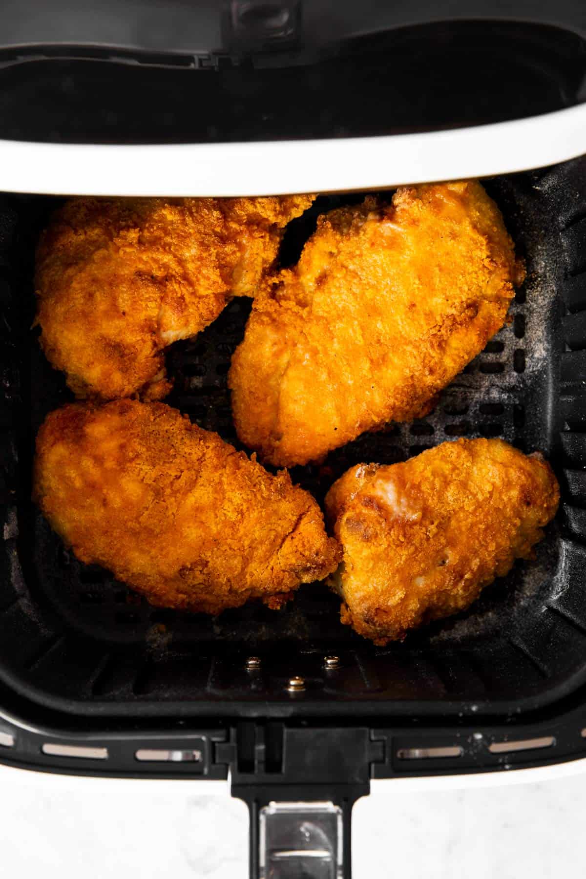 overhead view of four pieces of fried chicken in air fryer basket