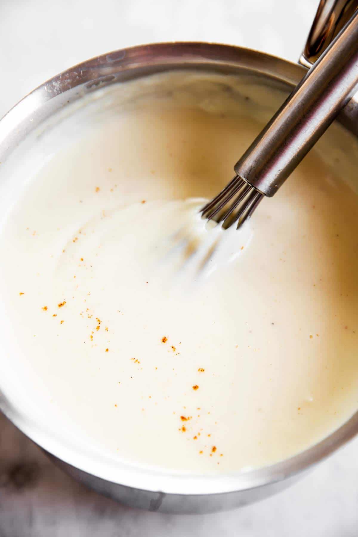 close up photo of whisk in saucepan with Béchamel sauce