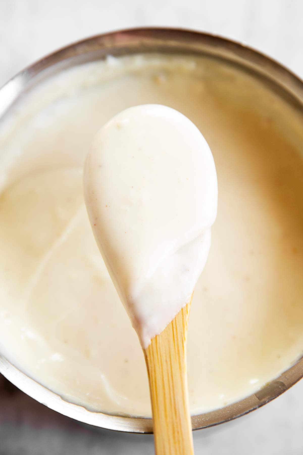 close up photo of béchamel sauce on wooden spoon