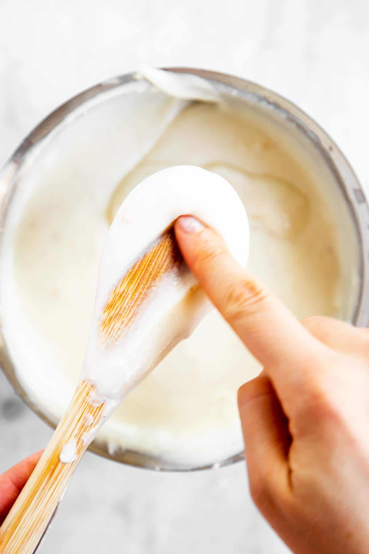 female hand stroking through Béchamel sauce coating back of a wooden spoon