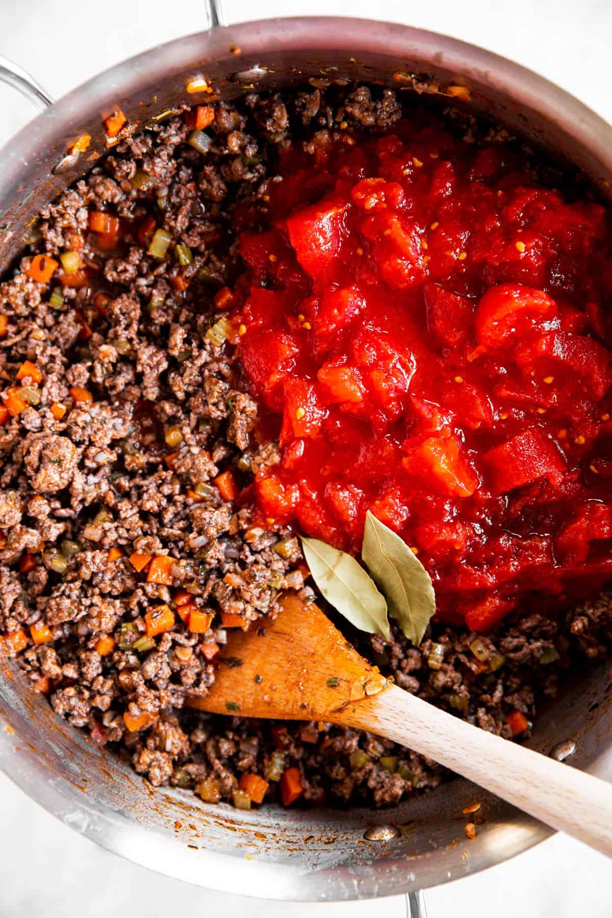 beef and vegetables for Bolognese sauce with crushed tomatoes in stainless steel skillet