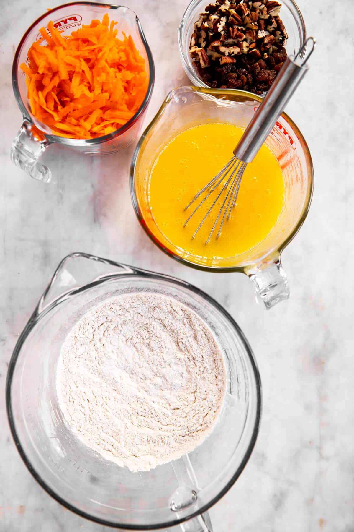 dry and wet ingredients for carrot muffins mixed in glass bowls, with mix-ins sitting next to bowls