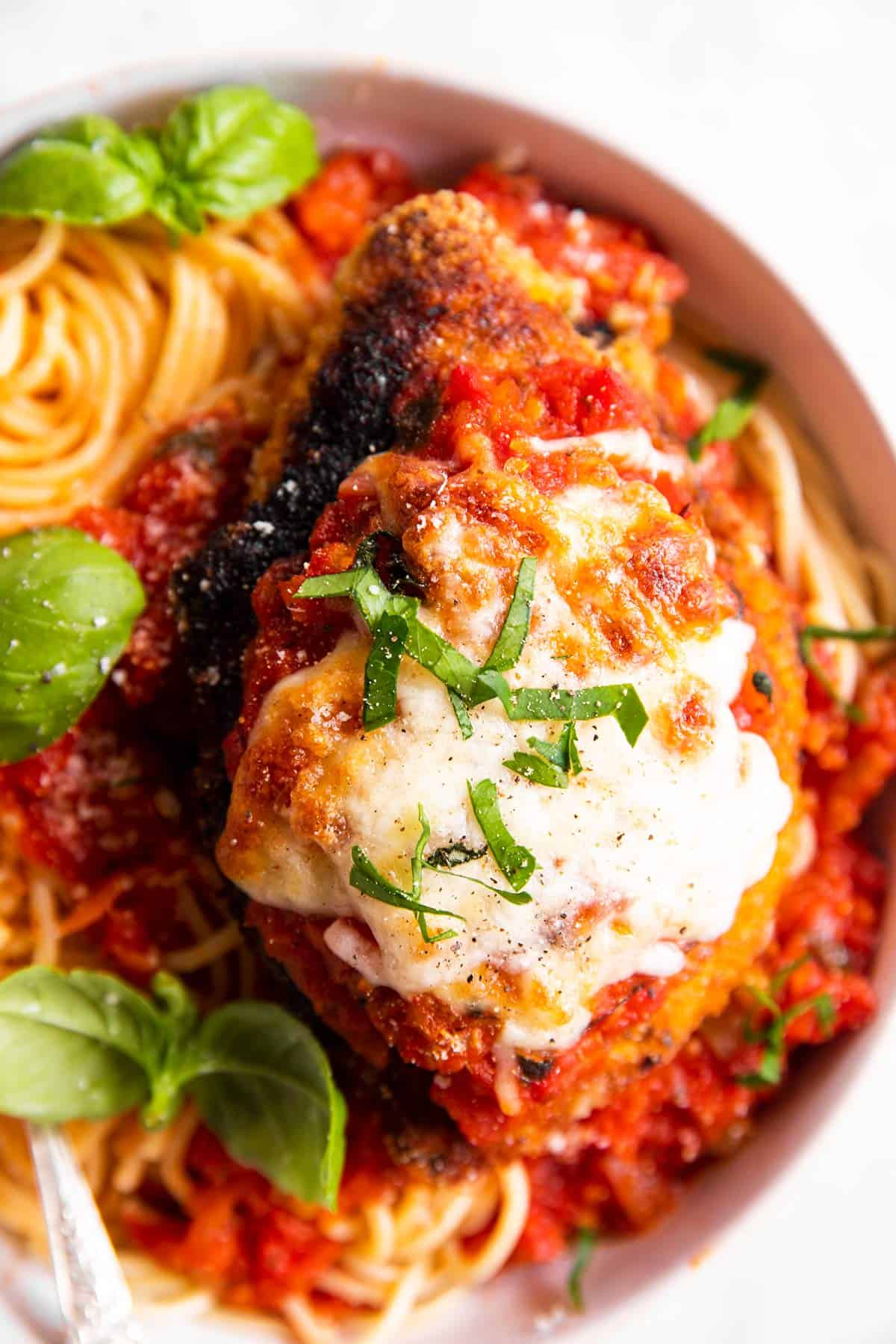 chicken parmesan on top of spaghetti in white bowl