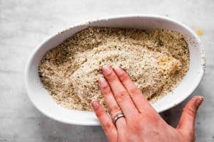 female hand pressing breadcrumbs on chicken breast