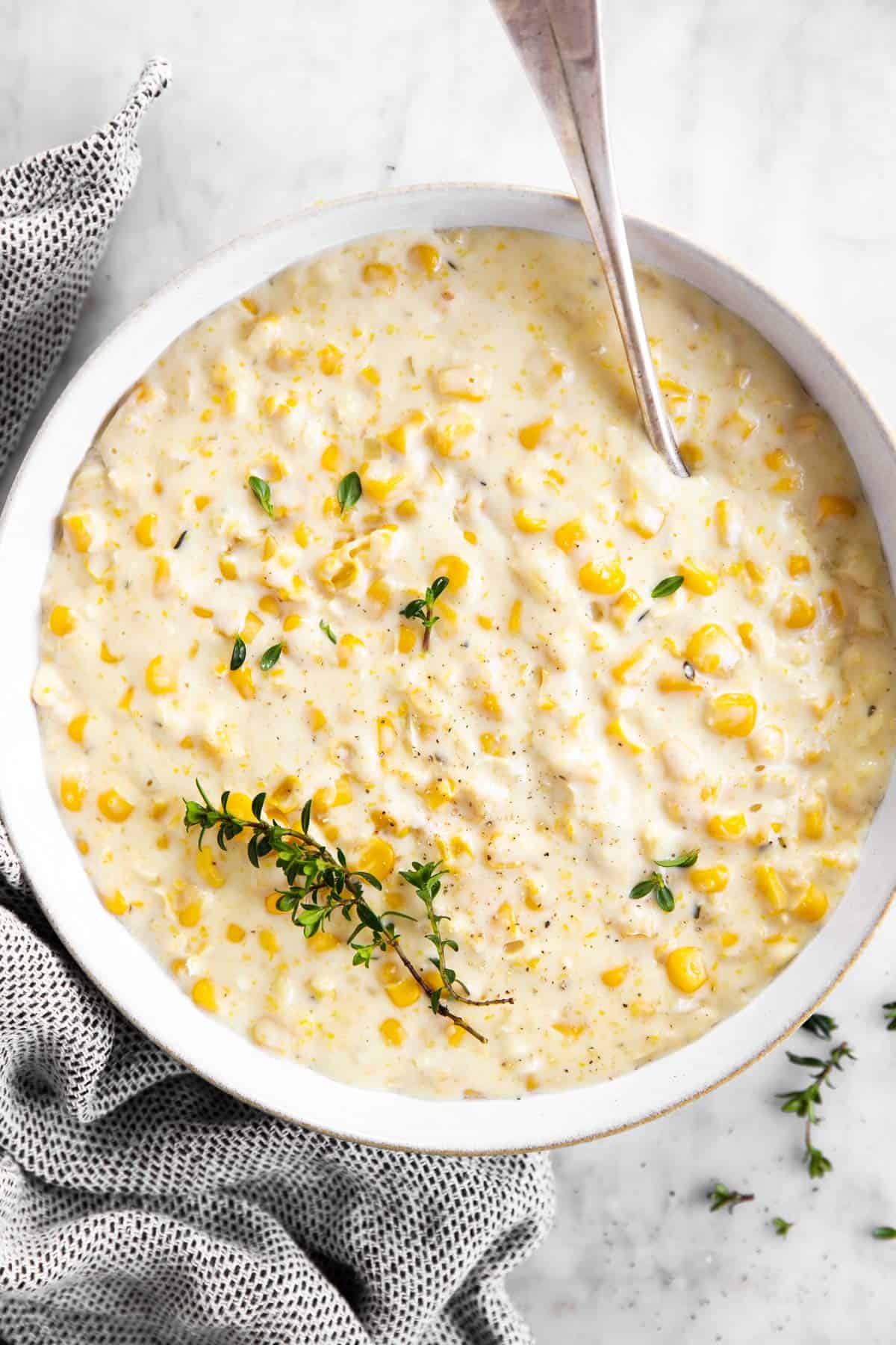 overhead view of white bowl filled with creamed corn and garnished with fresh thyme
