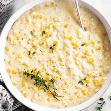 overhead view of white bowl filled with creamed corn and garnished with fresh thyme