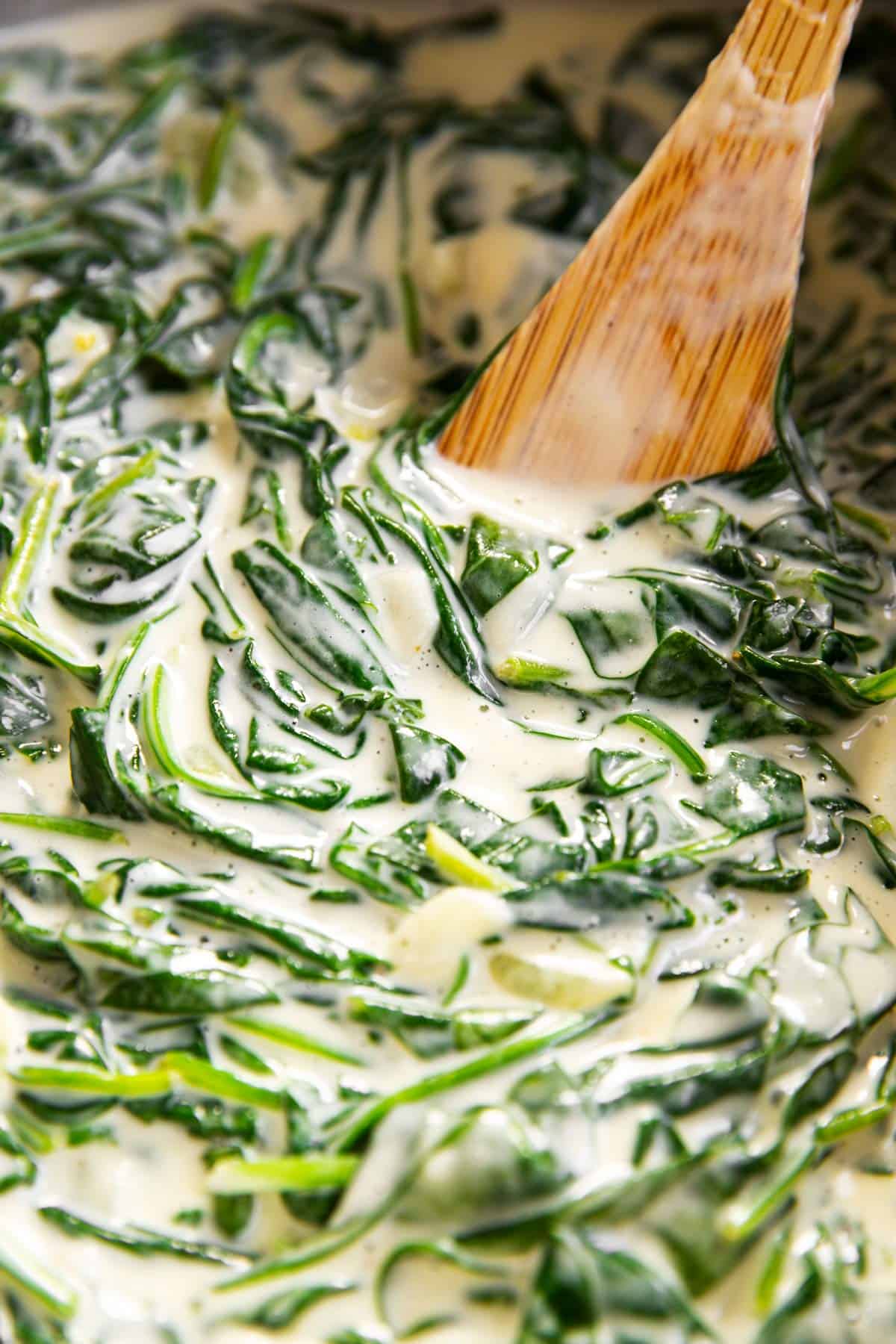 close up photo of creamed spinach in skillet with wooden spoon
