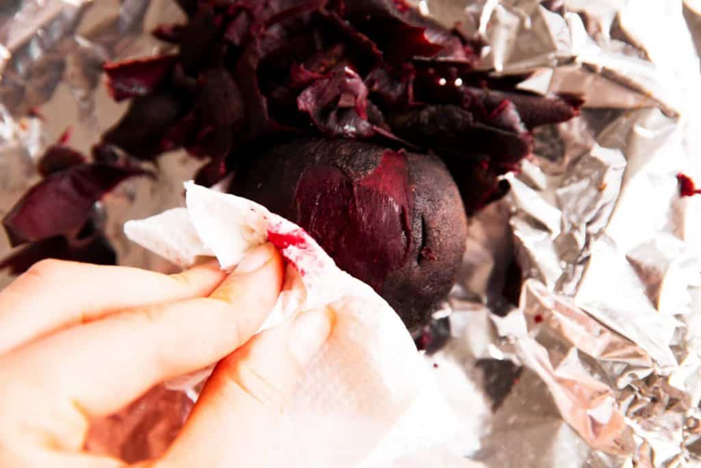 female hand scrubbing skin off of roasted beet