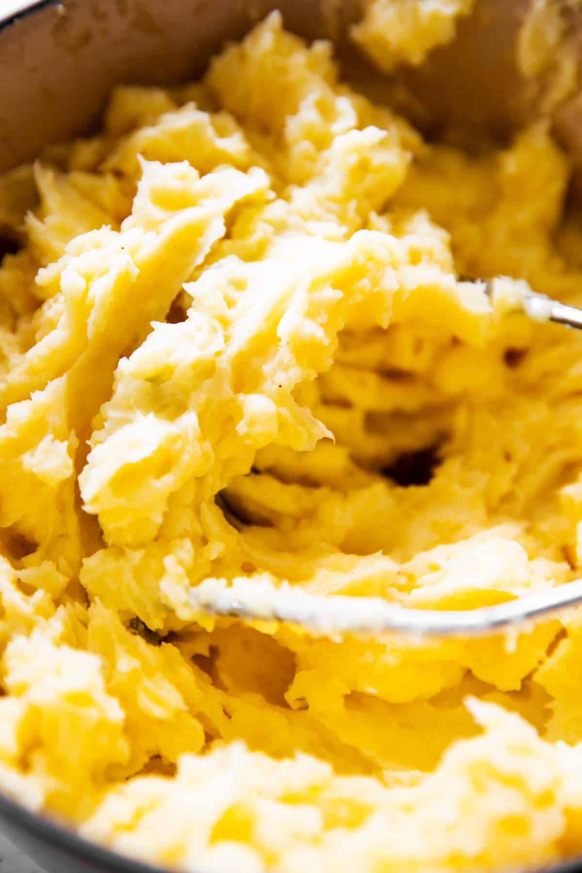 close up photo of potato masher in mashed potatoes