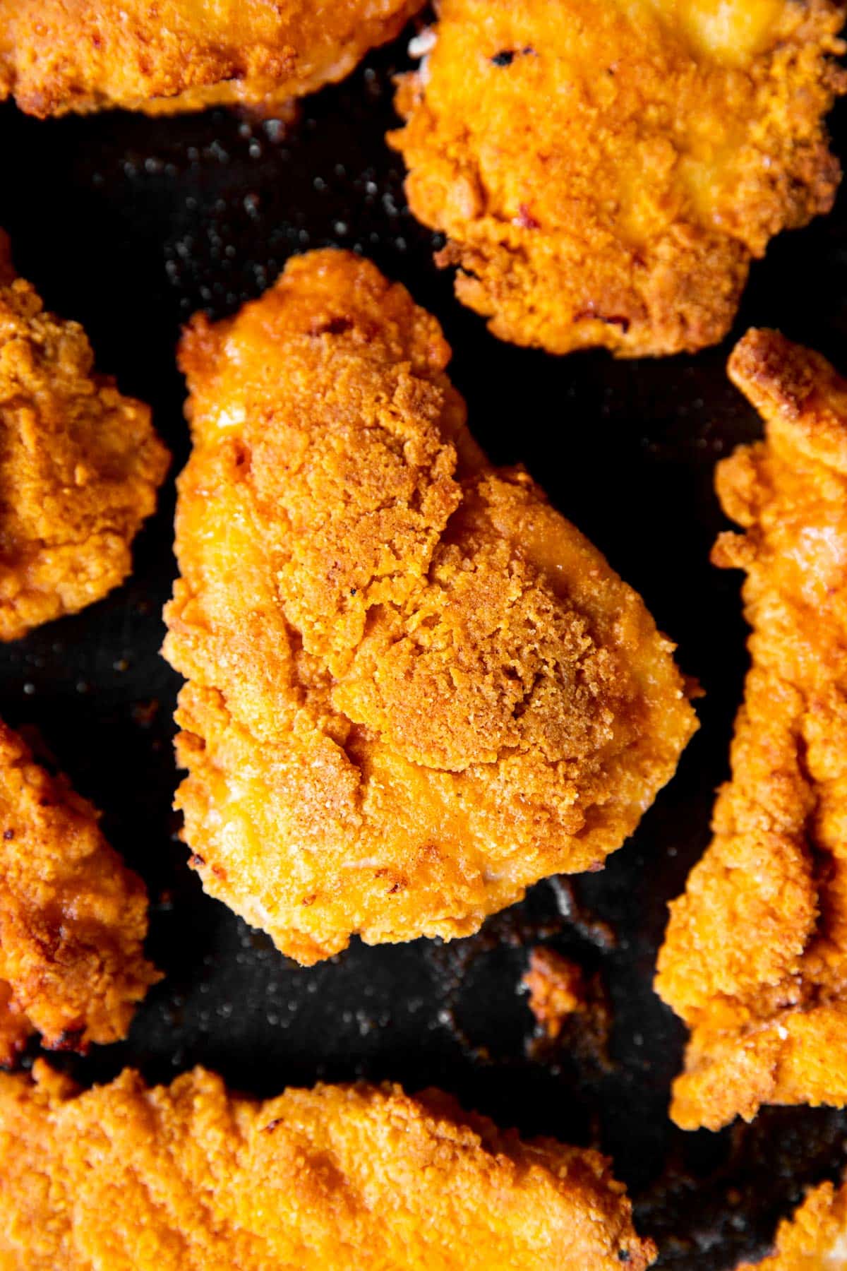 overhead close up photo of a piece of oven fried chicken on a black sheet pan