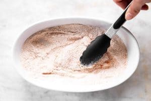 pounding chicken with breading with kitchen tongs