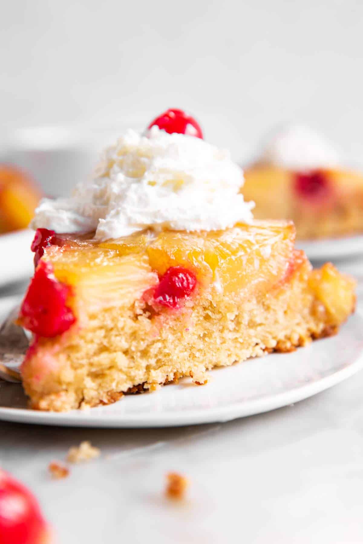 slice of pineapple upside down cake with whipped cream on white plate