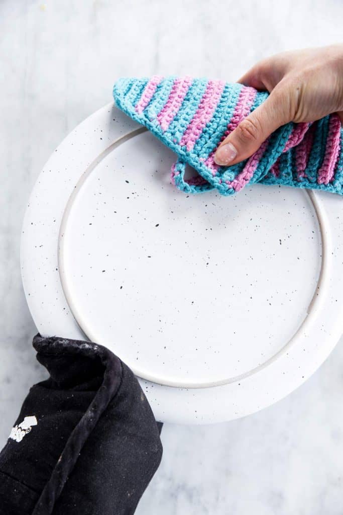 female hands holding plate with oven gloves on top of cake pan