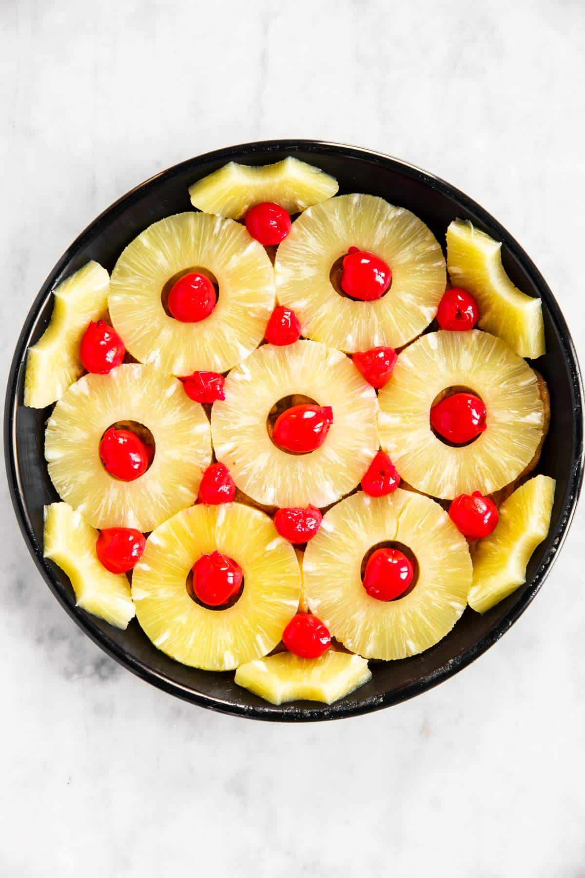 black cake pan lined with pineapple rings and maraschino cherries