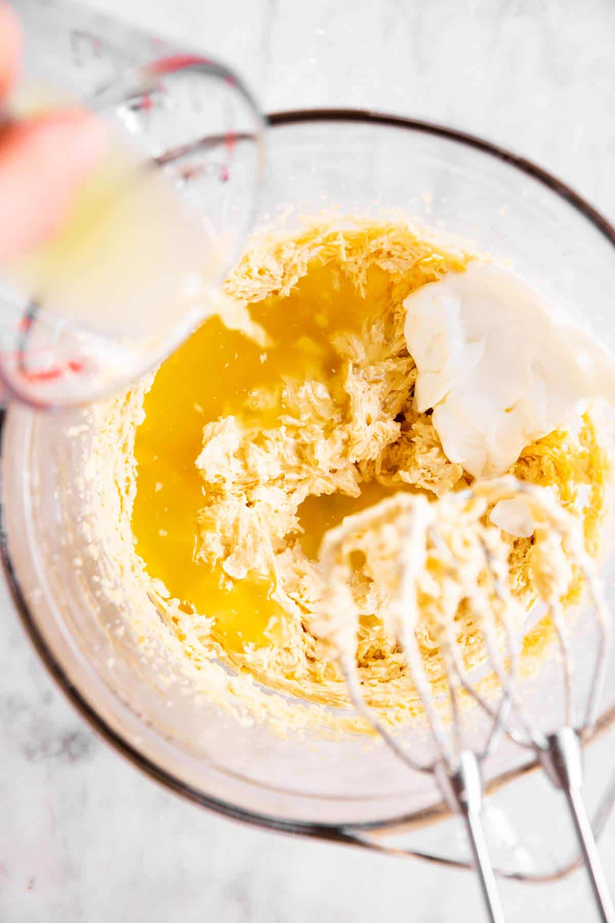 female hand pouring pineapple juice into bowl with creamed cake batter ingredients