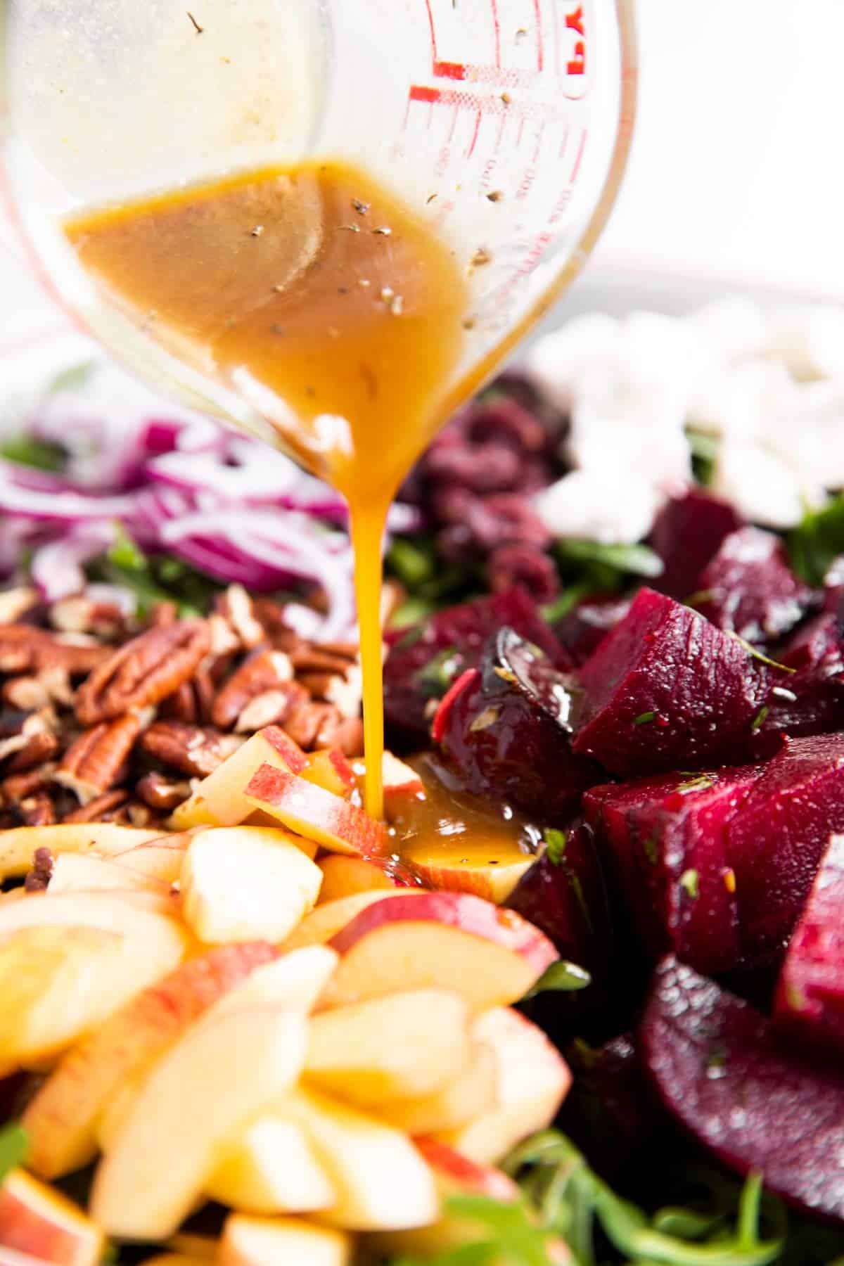 pouring salad dressing over ingredients for roasted beet salad