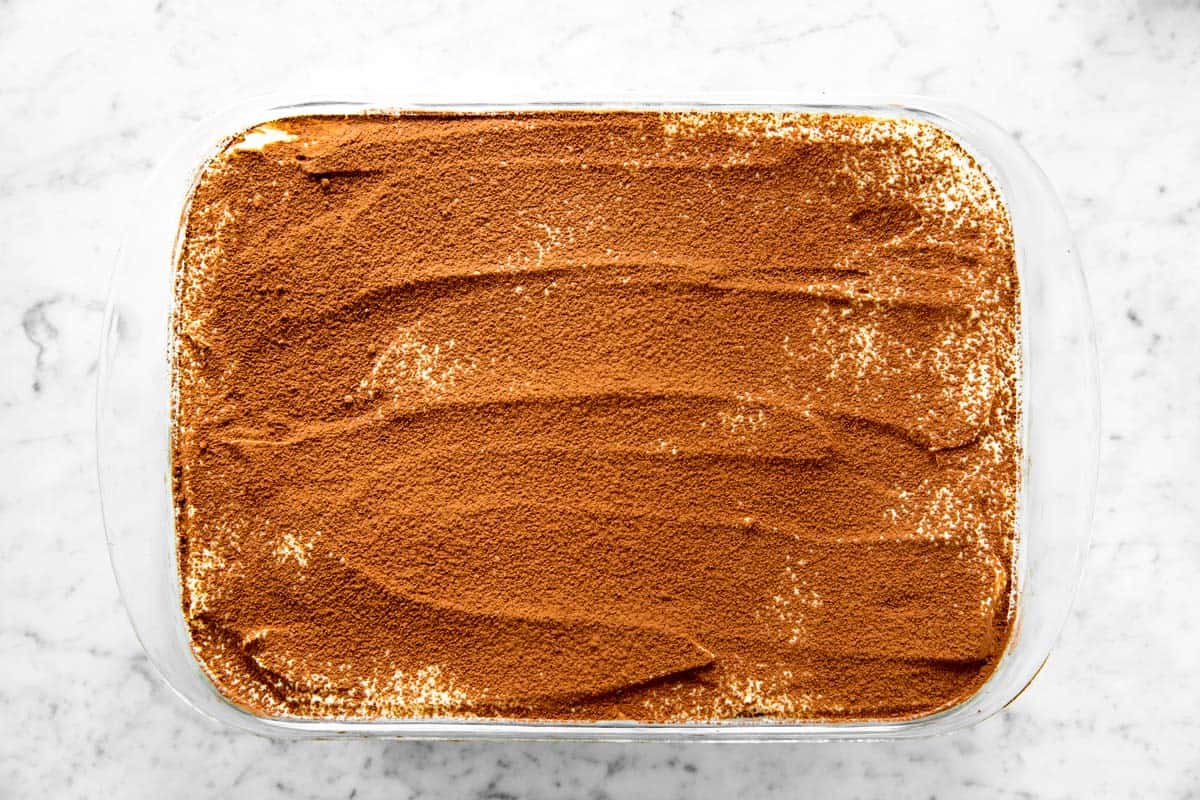 overhead view of tiramisu in glass pan dusted with cocoa powder