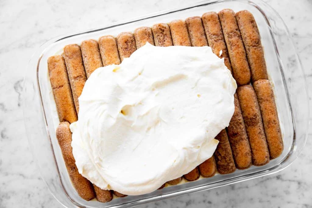 pan with half-assembled tiramisu and a blob of mascarpone cream on top