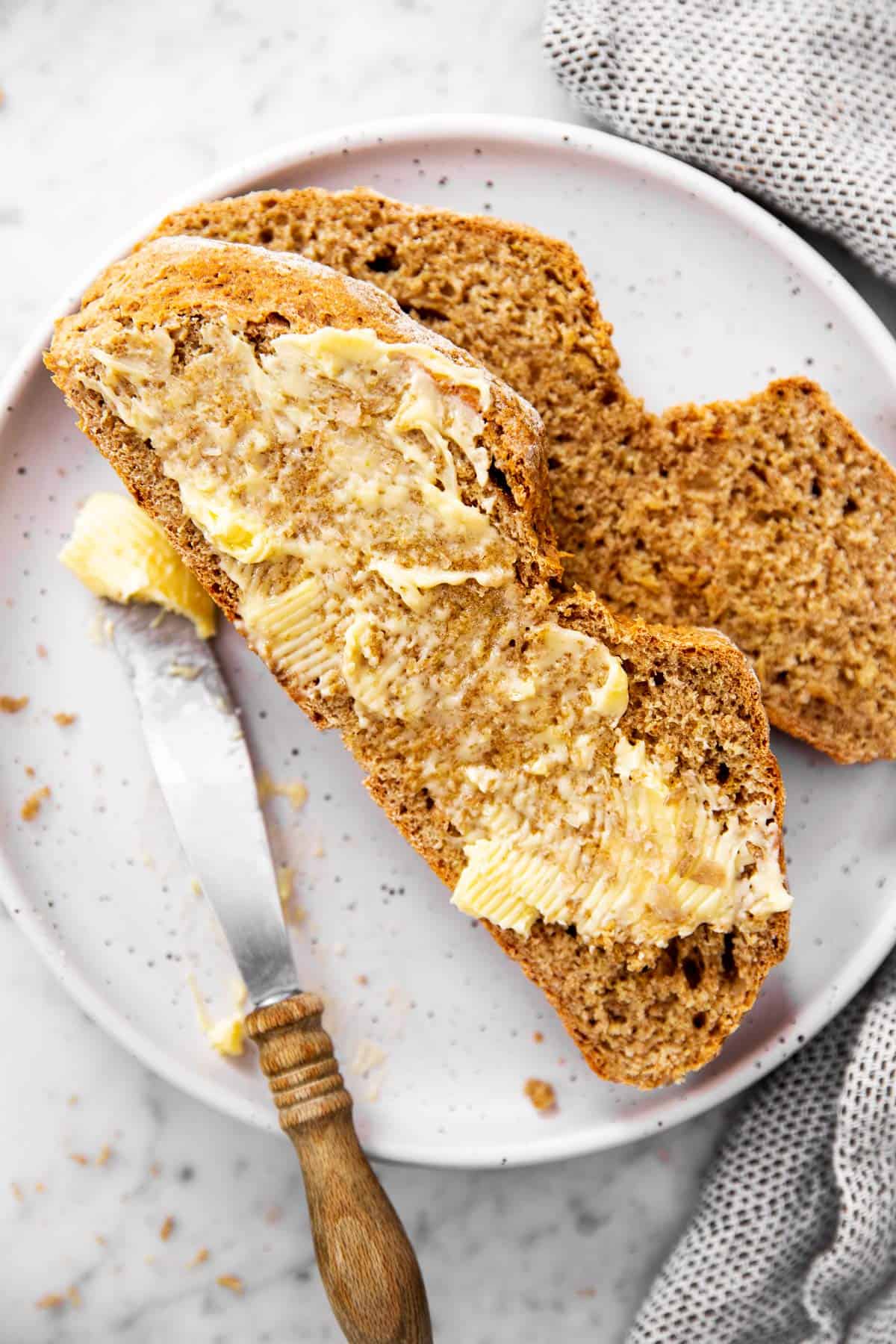 two slices of soda bread on white plate, one slice is buttered the other is plain