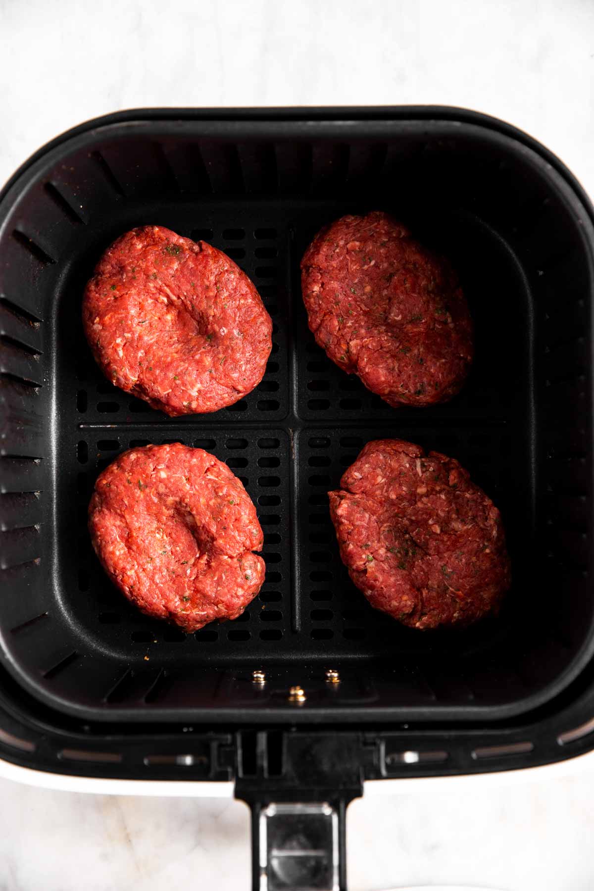 four raw burger patties in air fryer basket