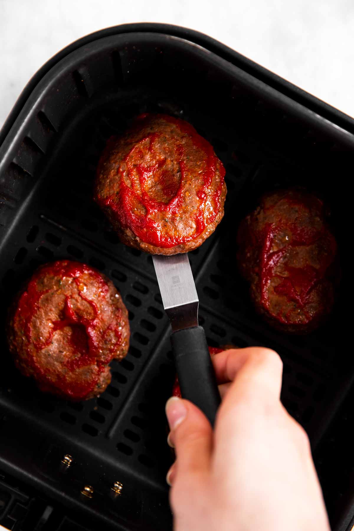 female hand flipping burger patty in air fryer basket