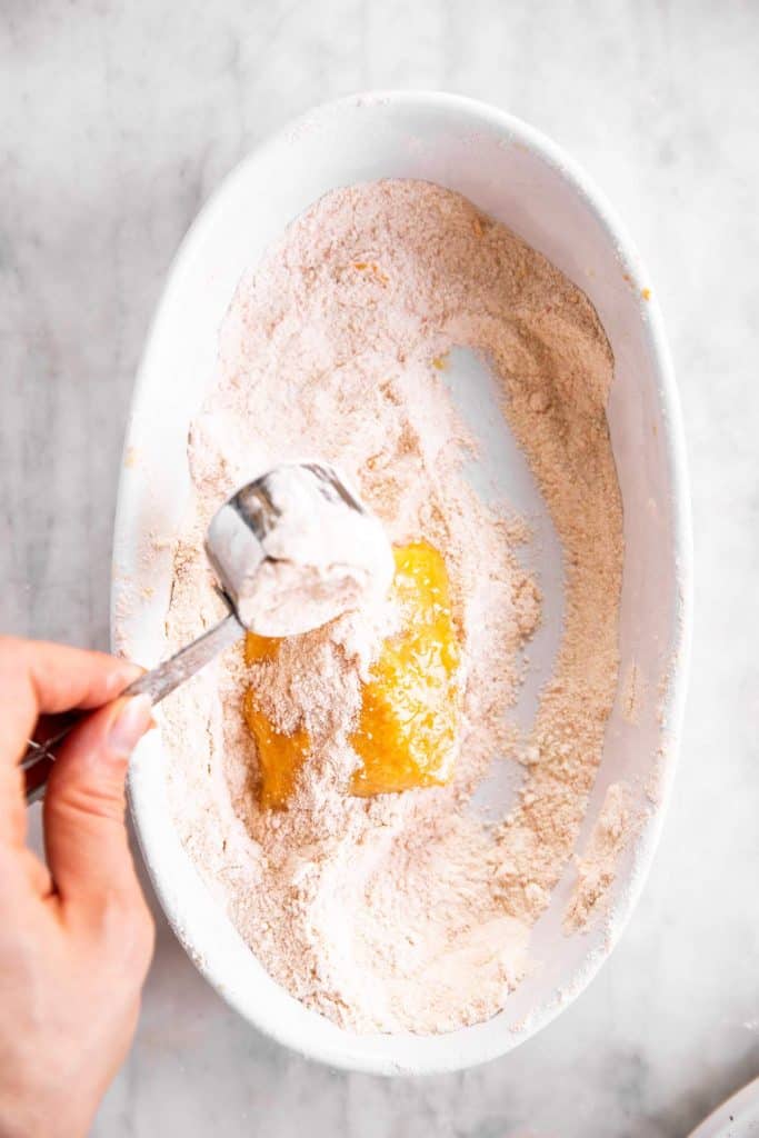 female hand scooping dry breading on top of egg washed fish fillet