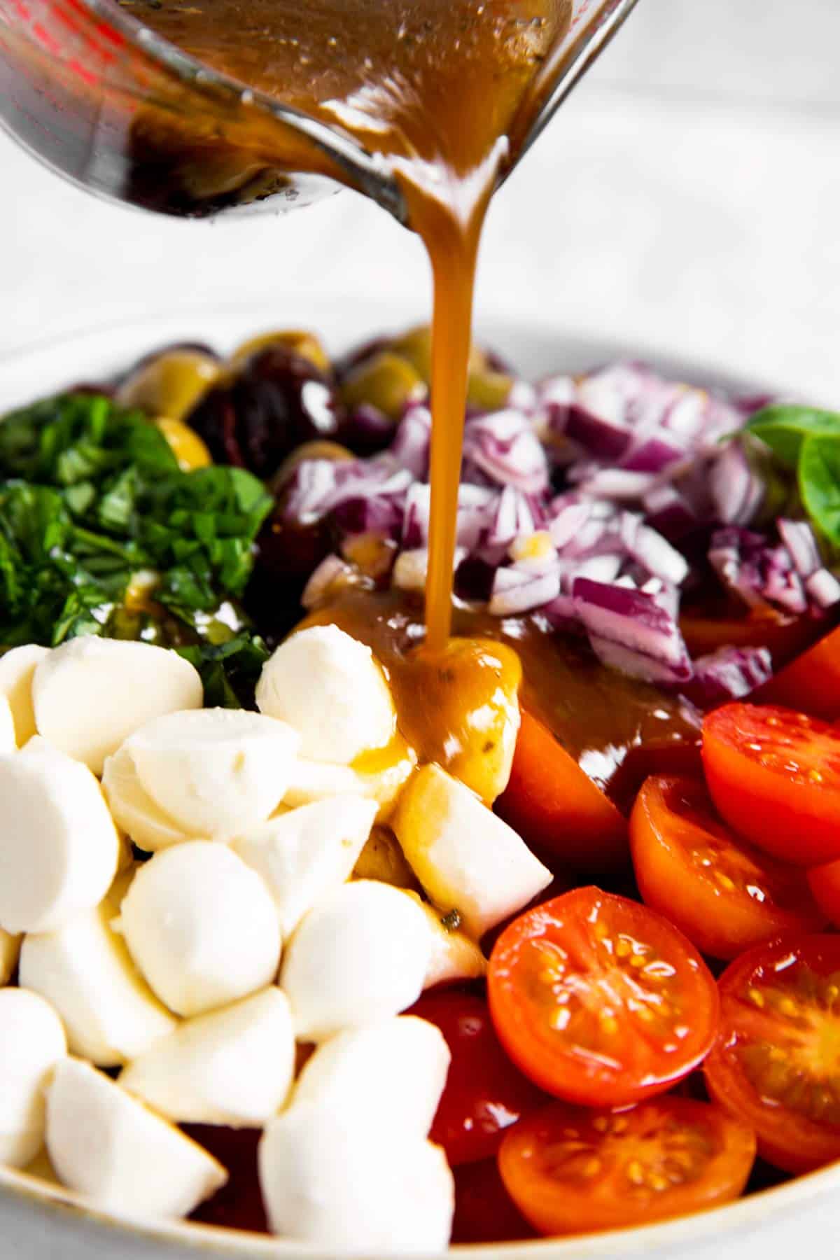 pouring balsamic vinaigrette dressing over ingredients for cherry tomato salad