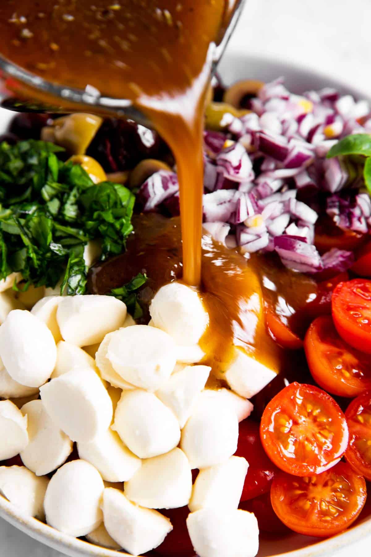 pouring balsamic vinaigrette dressing over cherry tomatoes and mozzarella balls