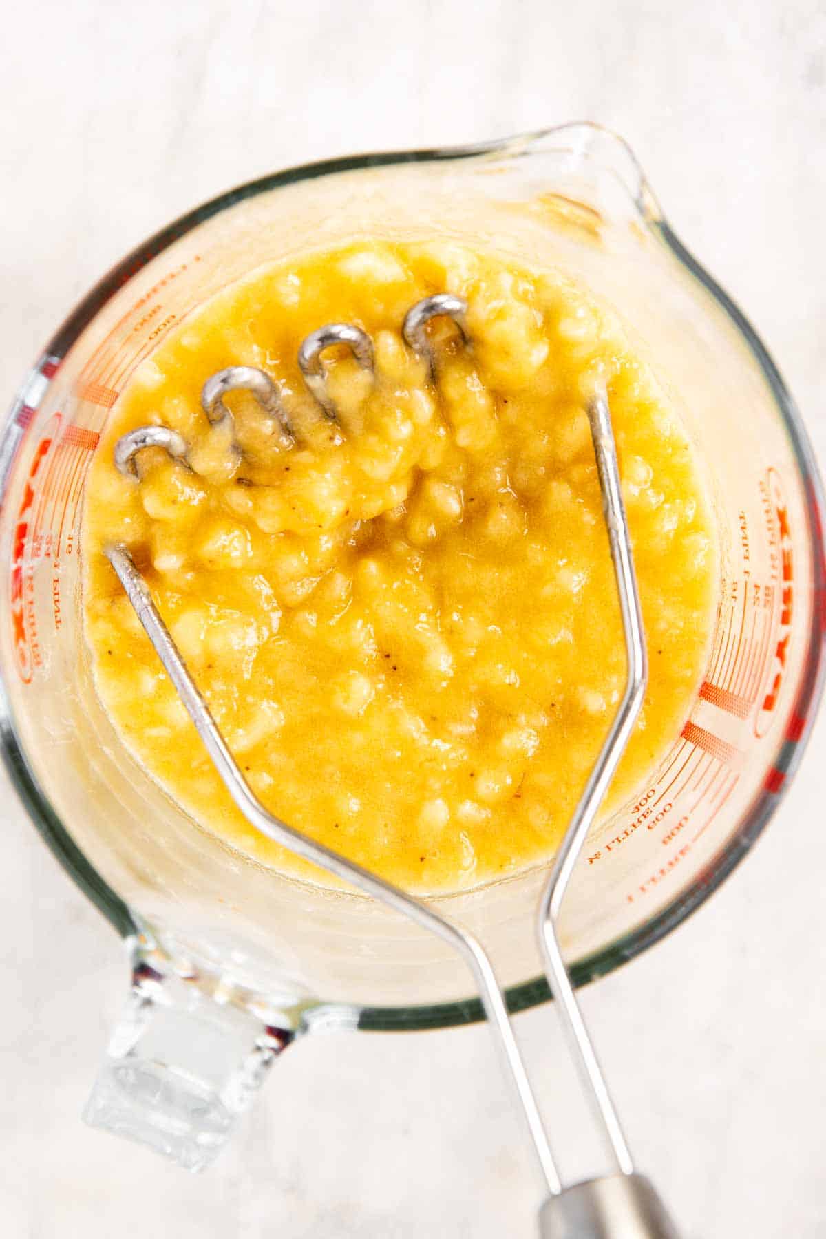 mashed bananas in glass emanating jug with potato masher