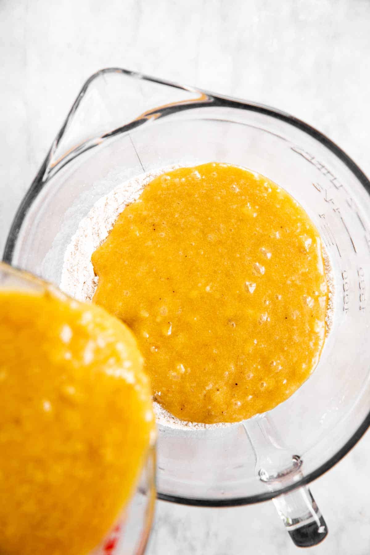 wet ingredients for banana bread pouring from glass measuring jug into glass mixing bowl