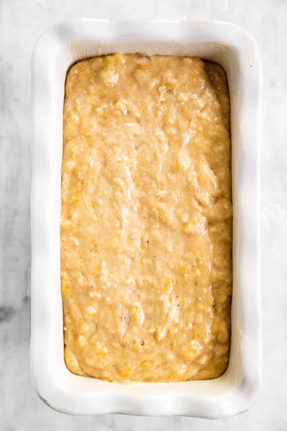 banana bread batter in white ceramic loaf pan sitting on marble surface