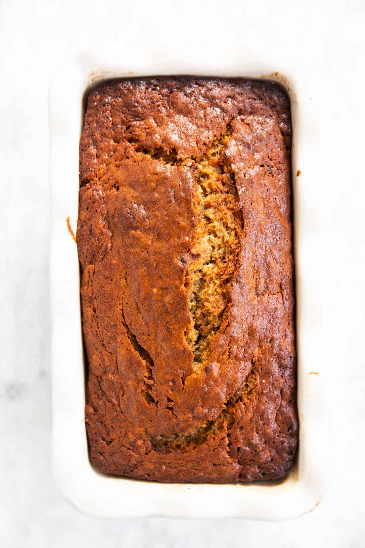 baked banana bread in white ceramic loaf pan sitting on marble surface