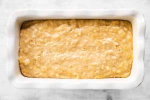 banana bread batter in white ceramic loaf pan sitting on marble surface