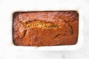 baked banana bread in white ceramic loaf pan sitting on marble surface