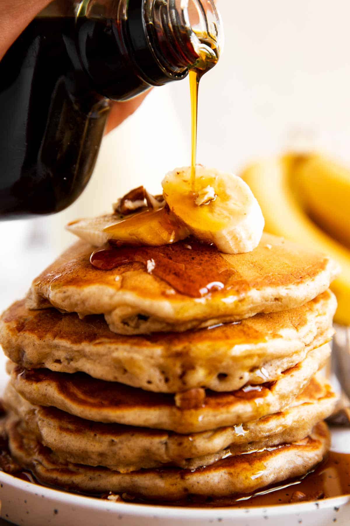 maple syrup pouring over stack of banana pancakes