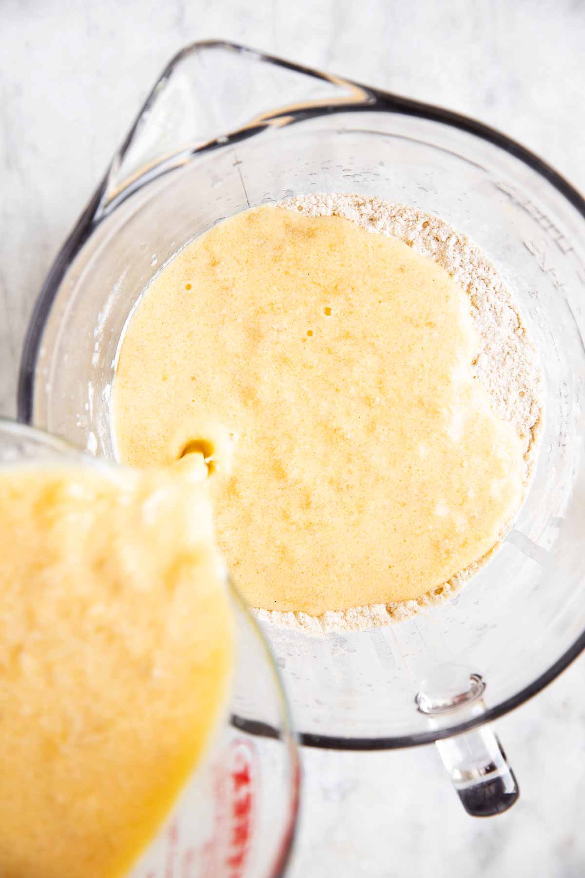 wet ingredients for banana pancake batter pouring from glass measuring jug into glass bowl with dry ingredients