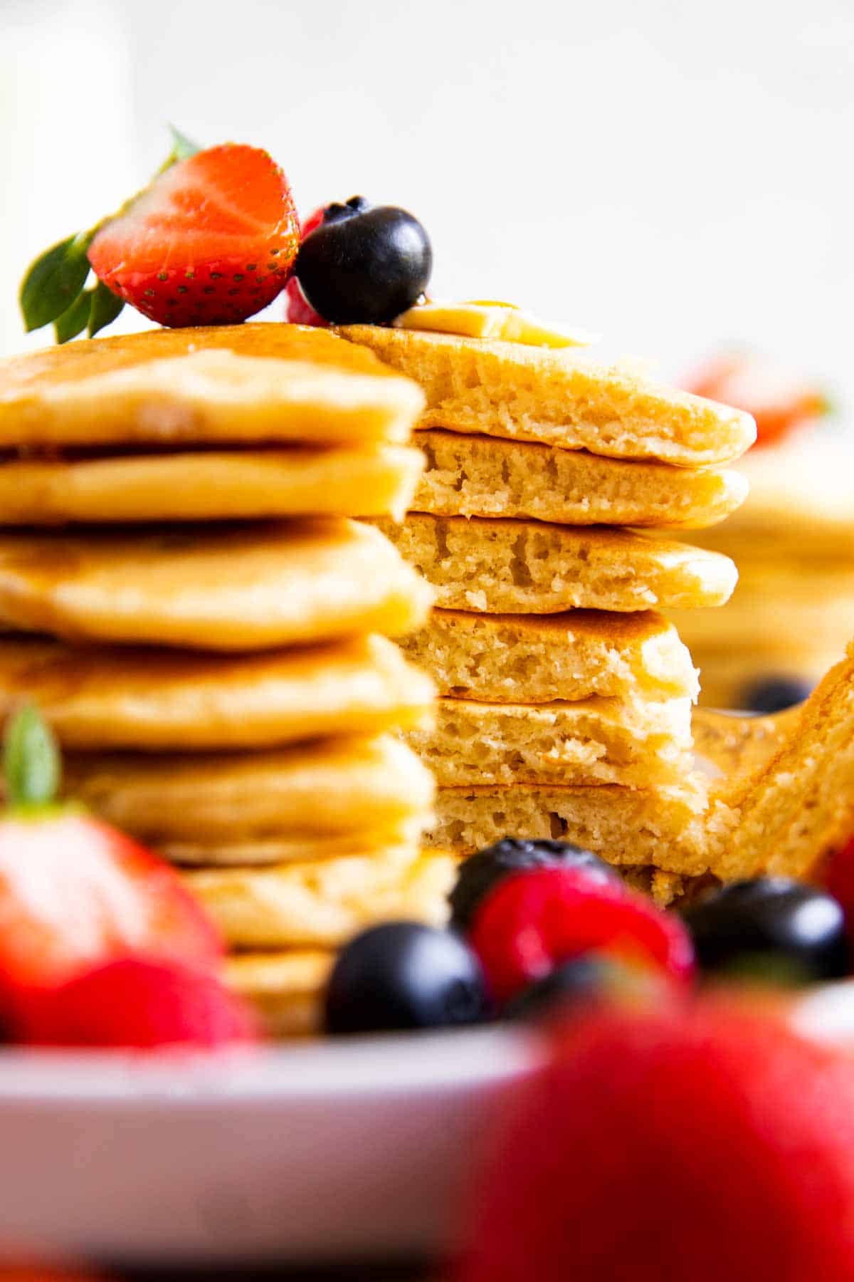 close up of stack of buttermilk pancakes garnished with fresh berries, with a wedge cut out
